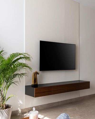 Wall-mounted TV on fluted white panel above a floating dark wood console with a brass horse figurine