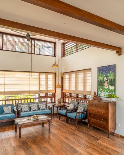 Living room with wooden beams, teal sofas, brass pendant lights, and a painted mural above a wooden dresser