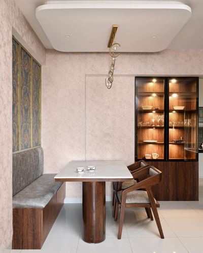 Dining nook with marble-top table on curved wood base, grey bench seating and lit wooden display cabinet
