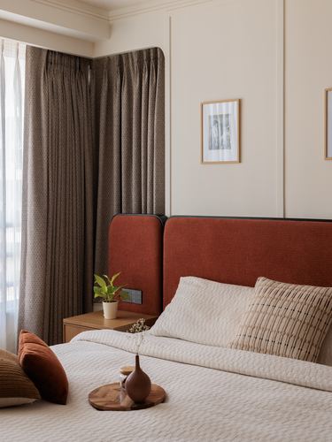 Bedroom corner with curved terracotta headboard, patterned curtains, and layered neutral bedding