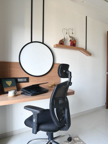 Study nook with wood desk, suspended round mirror, floating shelf and black ergonomic chair