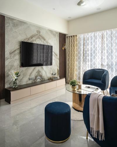 Living room with bookmatched stone tv wall, pink console, navy velvet chairs and pouf