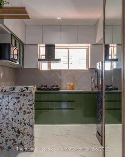 Modern kitchen with olive green glossy cabinets, terrazzo island, herringbone backsplash and window above sink