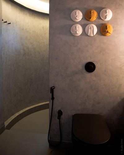 Curved plaster bathroom wall with six face-shaped wall sculptures above a black toilet and bidet spray
