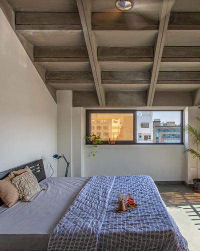 Bedroom with sloped exposed concrete beam ceiling, wooden bed, and window framing city view