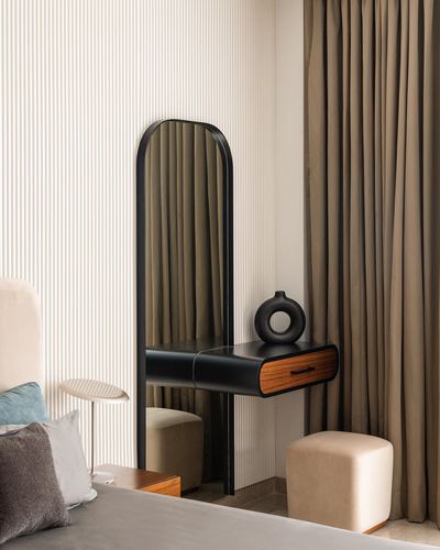 Black arched mirror with wood drawer beside bed, fluted wall and beige curtains