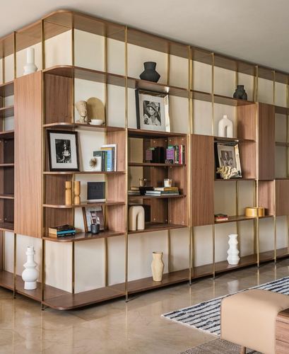 Curved walnut and brass display shelving unit filled with books and ceramics along a living room wall