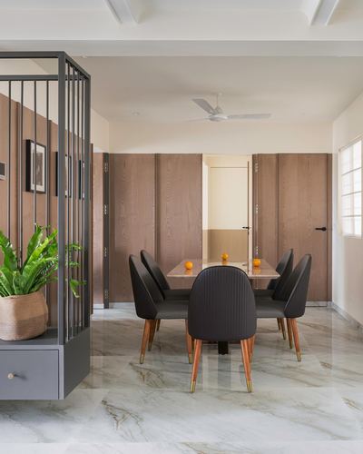 Dining area with marble-look table, black chairs, wood-panelled wall and metal screen divider in Pune apartment