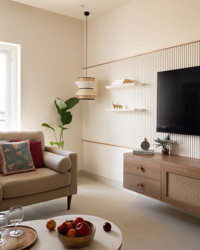 Beige living room with fluted wall panel, floating wood tv unit, cane detailing, and pendant light