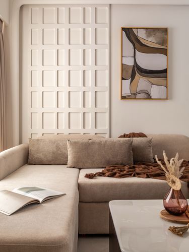 Beige sectional sofa against a raised grid-paneled wall with an abstract framed artwork above.