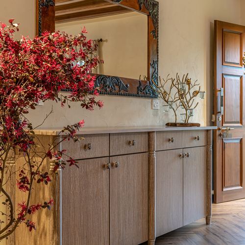 Entryway with carved mirror, wood sideboard, red floral arrangement and open panelled door