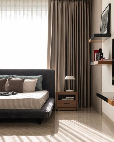 Bedroom with dark velvet bed, wooden nightstand, and sunlight filtering through curtains