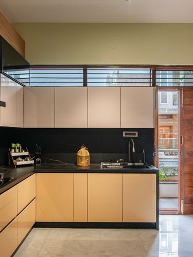 L-shaped kitchen with beige cabinetry, black stone counter, open wooden door to street