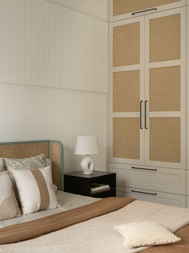 Bedroom corner with cane headboard, black nightstand, ceramic lamp and woven-panel wardrobe