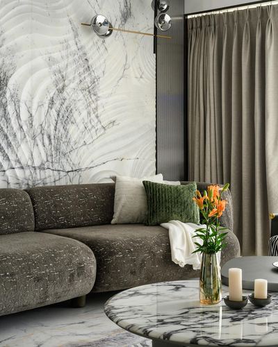 Grey textured sofa against a veined marble wall with beige curtains and a marble coffee table with flowers