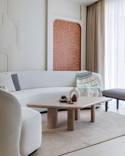Curved white sofa with beige coffee table, terracotta wall panel, and sheer curtains in a minimalist living room