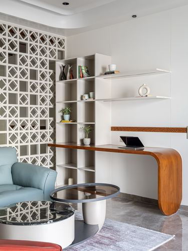 White study nook with jaali screen, cubby shelving, and a curved wood desk beside a blue sofa