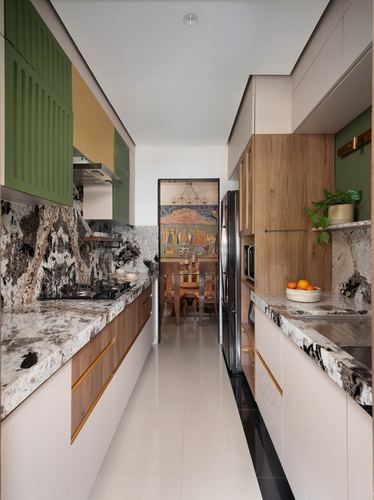 Galley kitchen with veined stone counters, wood and green cabinetry, dining area visible beyond