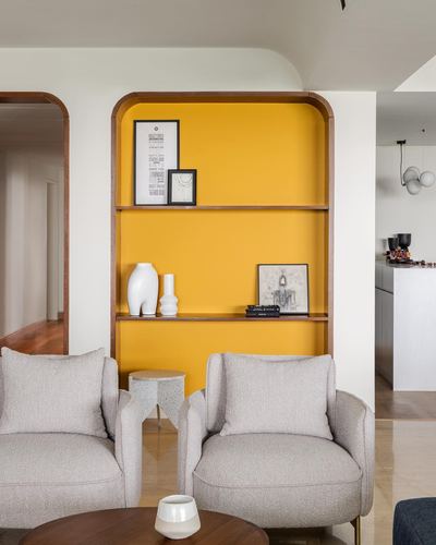 Grey boucle armchairs face an arched mustard shelving niche in a bright living room