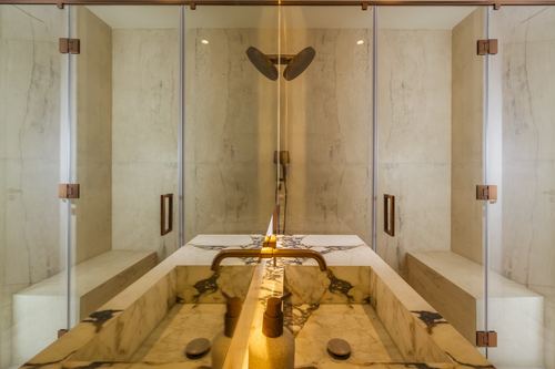 Symmetrical marble double vanity with bronze fixtures flanked by glass-enclosed shower stalls