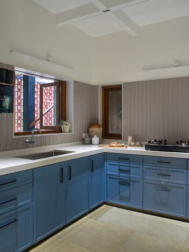 L-shaped kitchen with blue cabinetry, stone counters, ribbed tile backsplash and wooden window