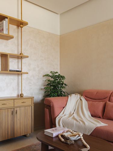 Terracotta sofa with throw blanket beside oak shelving and textured beige wall in living room