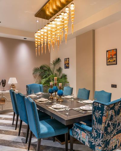 Dining room with teal velvet chairs, marble floor, and cascading amber glass chandelier over set table