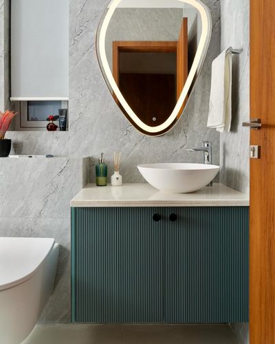 Grey marble bathroom with teal fluted vanity, white vessel sink, and backlit organic mirror
