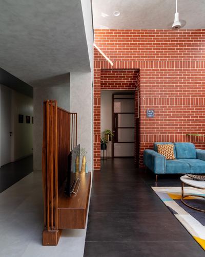 Living room with red exposed brick wall, teal sofa, and wooden slatted partition dividing corridor
