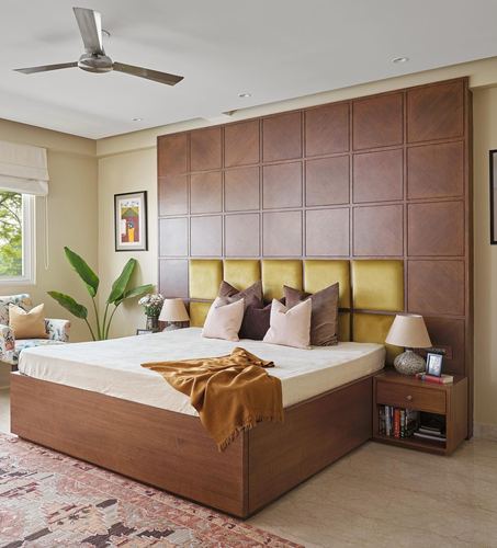 Bedroom with wood-panelled headboard wall, mustard upholstery, and layered cushions on a king bed