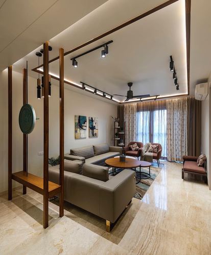 Living room with grey sectional sofa, wooden ceiling frame, and stone flooring under warm lighting
