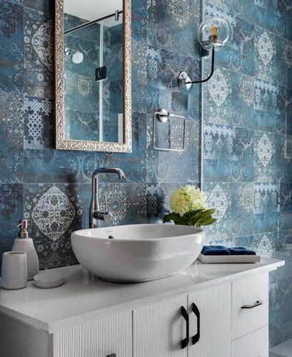 White vessel sink on marble counter against patterned blue mosaic tile wall with gold mirror