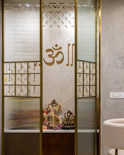 Pooja unit with brass om symbol, hanging bells, and deity idols behind fluted glass doors