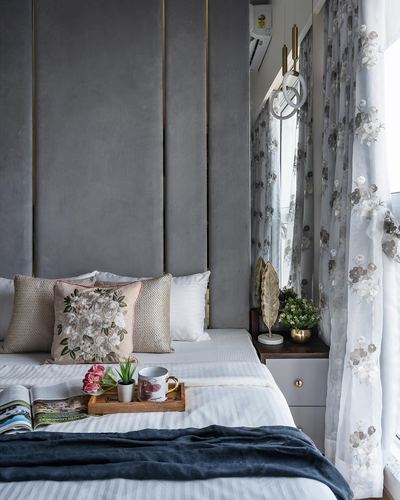Grey velvet-panelled headboard wall with brass lines, floral cushions and sheer floral curtains by window