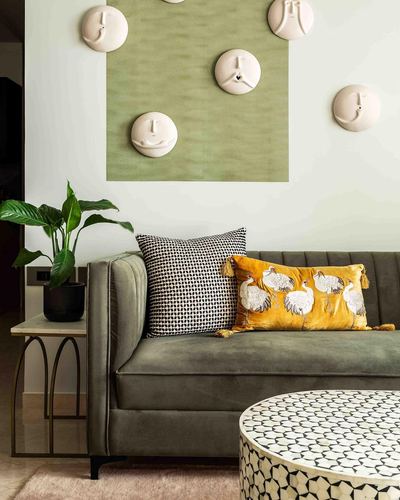Olive velvet sofa with patterned cushions beneath ceramic face wall art in Mumbai living room