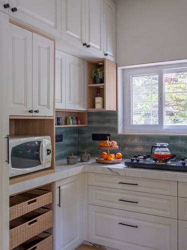 Corner kitchen with white panelled cabinetry, wood-toned open shelving, teal tile backsplash, and marble-look counter under a window