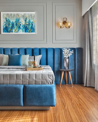 Blue velvet channel-tufted headboard bed with wooden floor and gray paneled wall