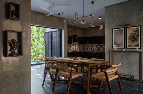 Dark-toned dining room with cane chairs, patterned tile kitchen, and glass doors to garden pool