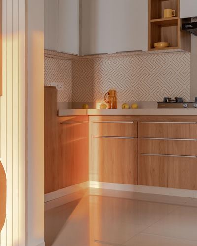 Warm-toned kitchen corner with wood cabinets, patterned tile backsplash, lit by strong diagonal sunlight