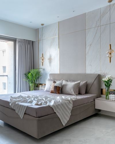 Bedroom with taupe velvet bed, marble panelled wall with brass inlay, two globe pendant lights