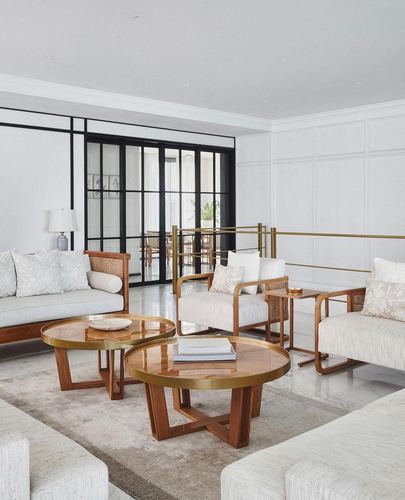 Ivory living room with cane armchairs, round brass-trimmed wood coffee tables and black-framed glass doors