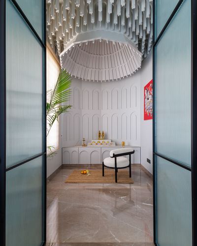 Pooja room seen through fluted glass doors, arched white panelling and sculptural ceiling fixture above marble floor