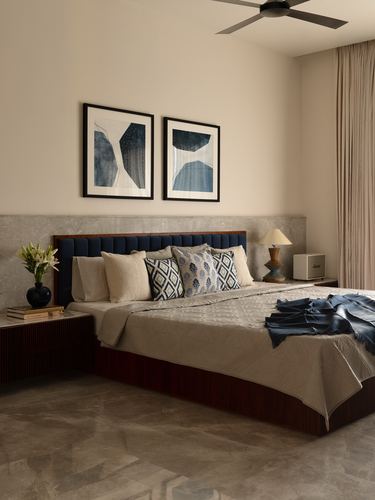 Bedroom with navy tufted headboard, stone wall panel, twin abstract artworks and marble flooring