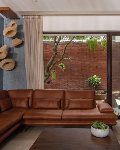 Living room with tan leather sofa facing glass wall onto brick courtyard with tree