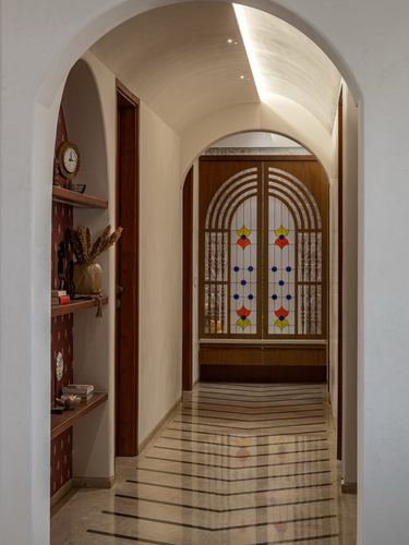 Arched corridor with barrel ceiling leading to a stained glass temple door in a Vadodara home