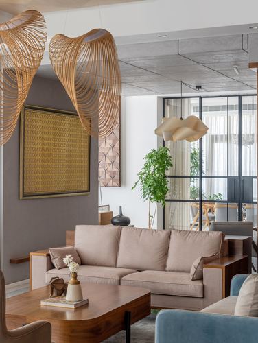 Living room with woven rattan pendant lights, taupe sofa, wood coffee table, and glass partition to dining area