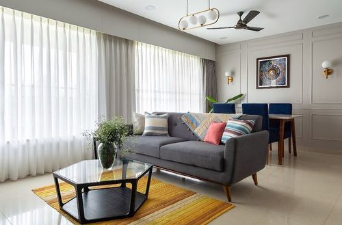 Grey living room with sheer curtains, blue sofa pillows, hexagonal glass coffee table on mustard rug
