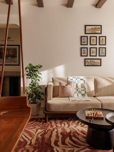 Living room corner with wooden swing, beige sofa, gallery wall, and striped rug in warm light