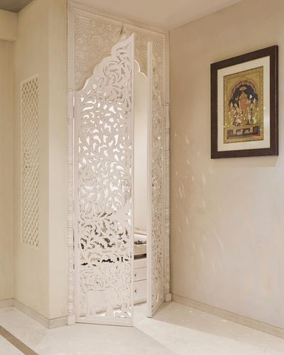 White carved wooden jali door with floral and elephant motifs beside a framed miniature painting in a beige foyer
