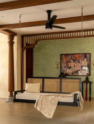 Black cane-panelled hanging daybed swing in a Chennai living room with green textured wall and painting
